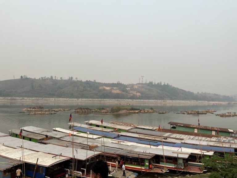 Docked longboats on a hazy river, 2024 slow boat still leaving from here, NOT from new slow boat pier, Houayxay, Bokeo Province, Laos.
