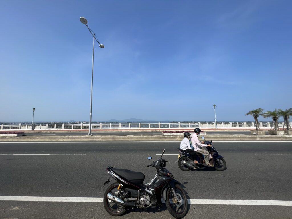 Motorcycles on a sunny road with a bridge, Đà Nẵng, Vietnam.