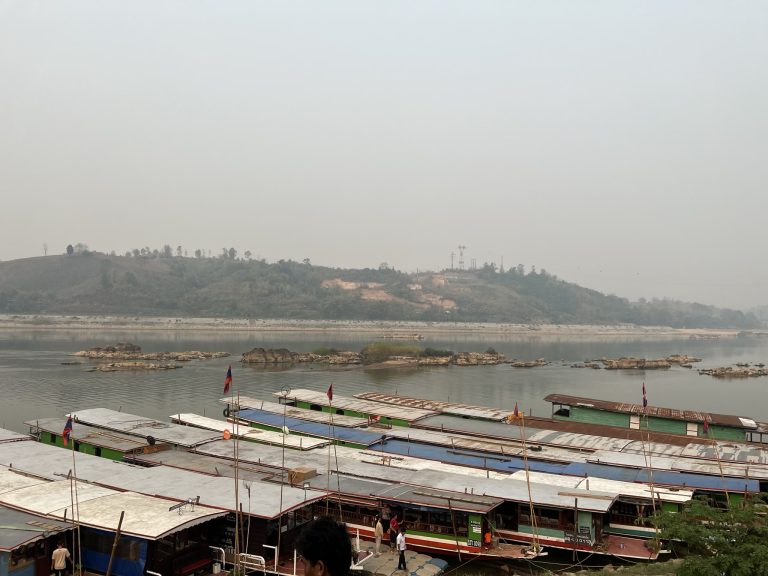 Docked longboats on a hazy river, 2024 slow boat still leaving from here, NOT from new slow boat pier, Houayxay, Bokeo Province, Laos.